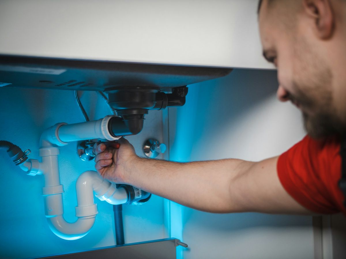 Een loodgieter draait de sifon onder een lavabo los